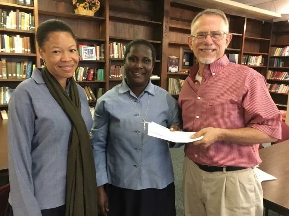 Three people smiling indoors, with a man holding a document in a library.