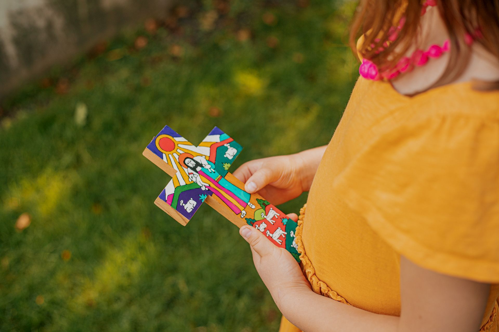 Person in a mustard shirt holding a colorful homemade paper craft outdoors on grass