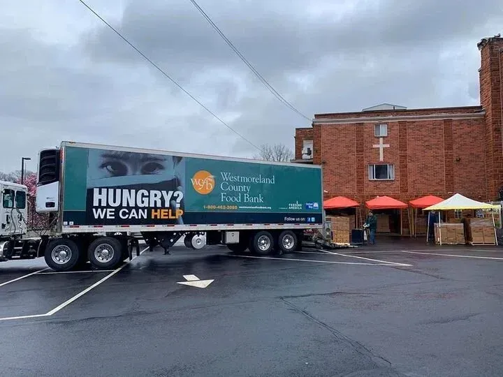 Food bank truck parked outside a brick building in the rain, with “HUNGRY? WE CAN HELP” on the side.