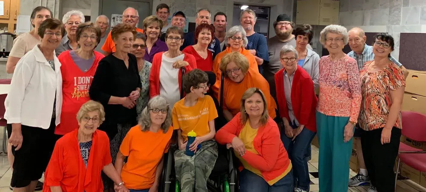 Large group posing indoors, many wearing orange shirts and smiling at the camera.