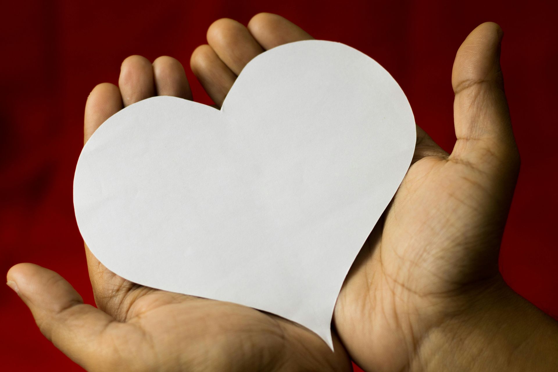 Hands holding a white heart cutout against a red background