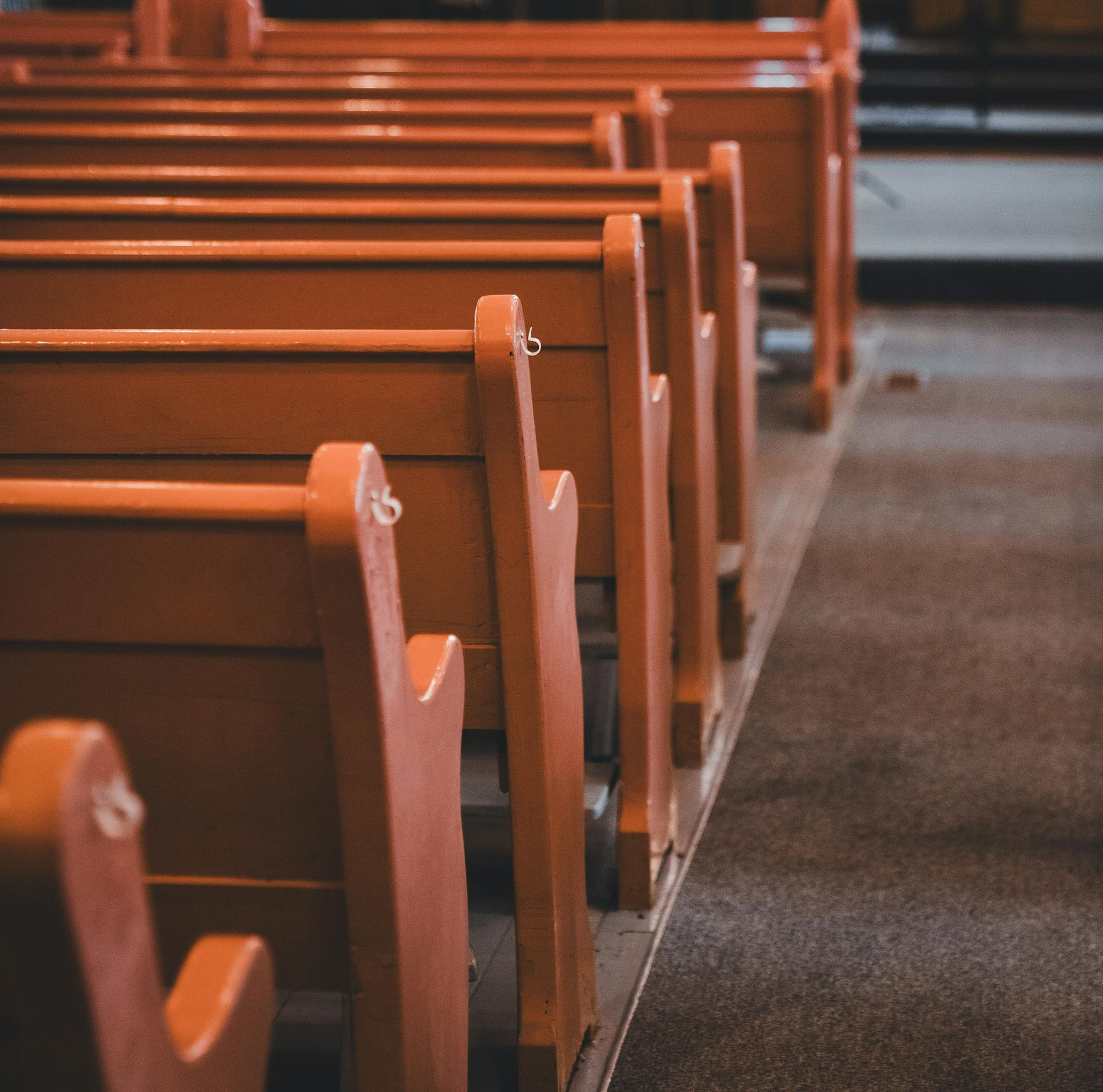 Rows of empty wooden church pews beside a carpeted aisle