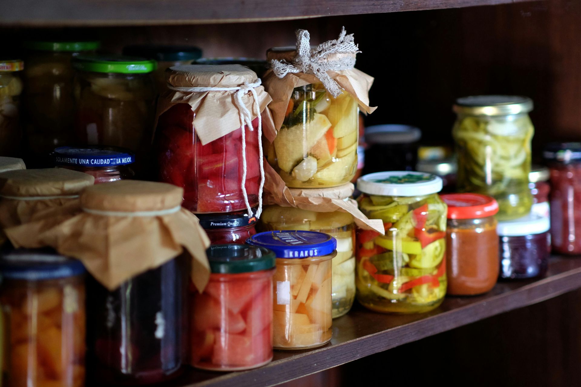 Assorted homemade preserves and pickled vegetables in jars on wooden shelves