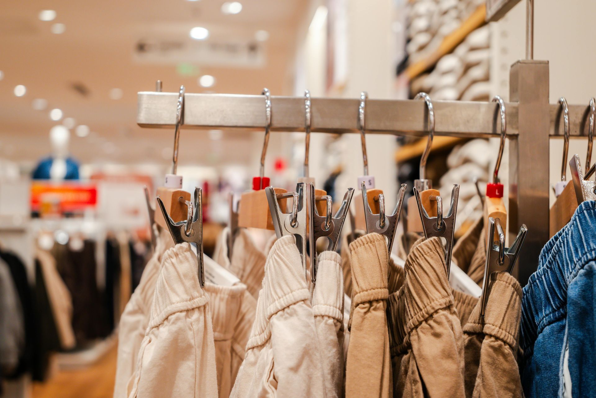 Clothing store rack with beige jackets and blue denim hangers under warm lights