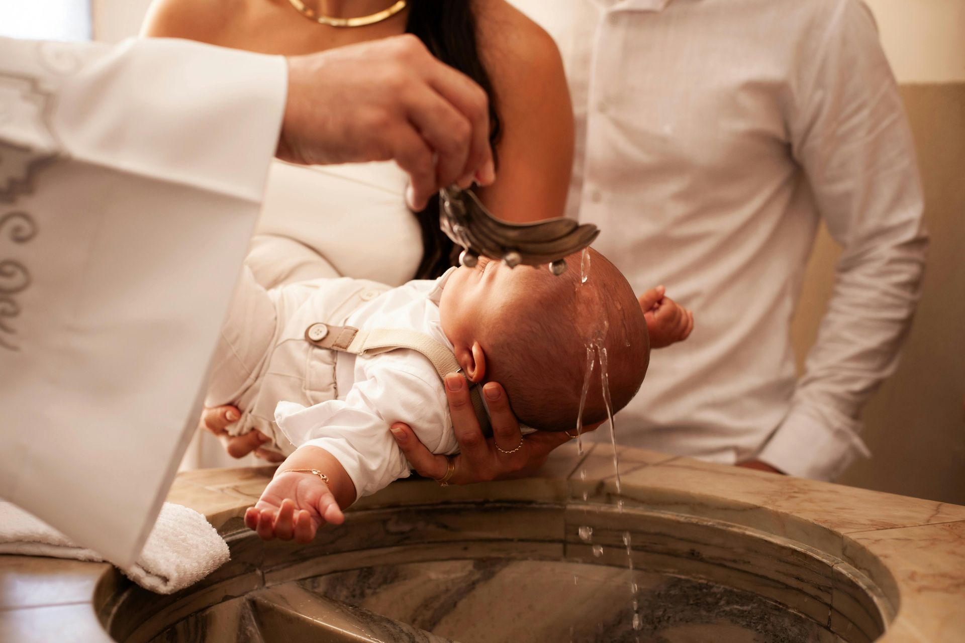 Baby being baptized over a stone font, with water poured from a shell in a church ceremony
