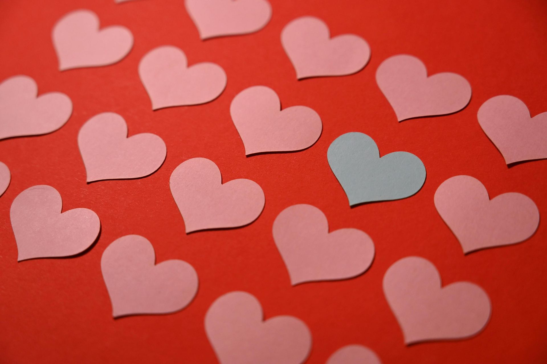 Pink paper hearts scattered on a red background, with one light blue heart among them