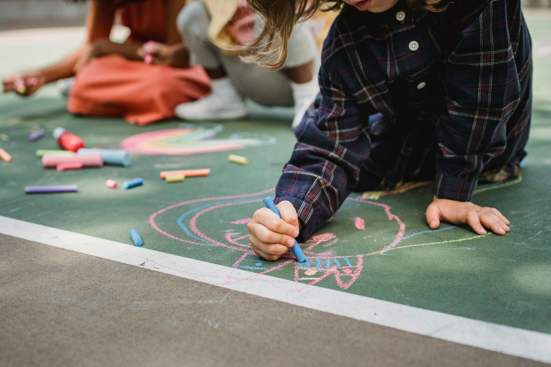 Child drawing colorful chalk art on a green playground surface