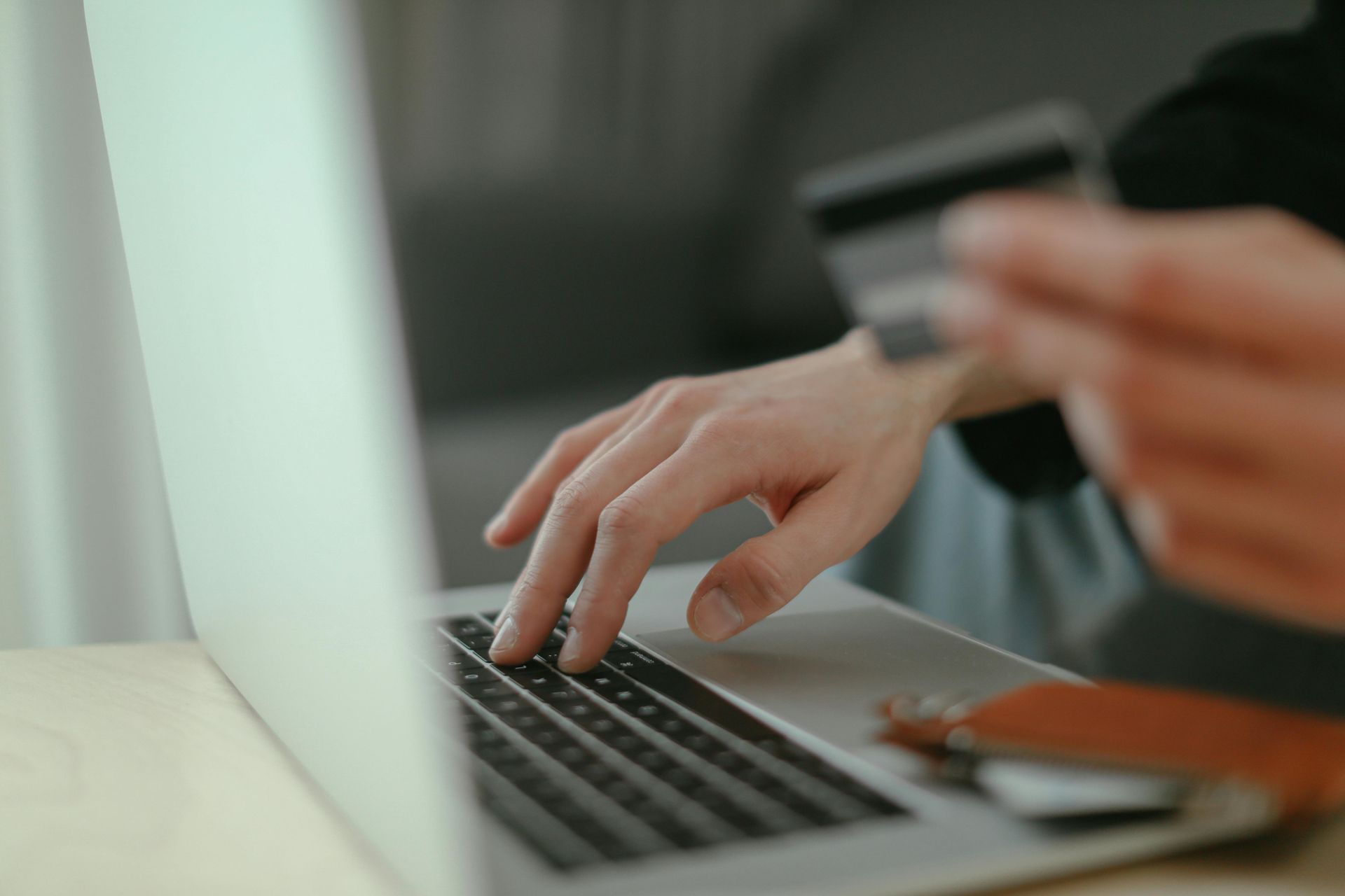 Hands typing on a laptop keyboard beside a smartphone and notebook on a desk.