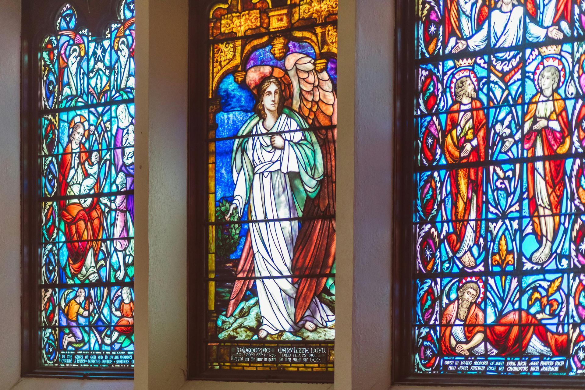 Three stained-glass church windows with biblical figures in blue, red, and gold panels