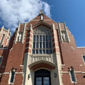 Red brick church facade with tall arched stained-glass window under a blue sky