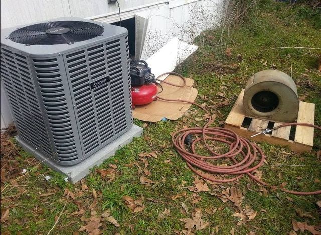 Outdoor HVAC unit with coiled hoses and tools on grass beside a house
