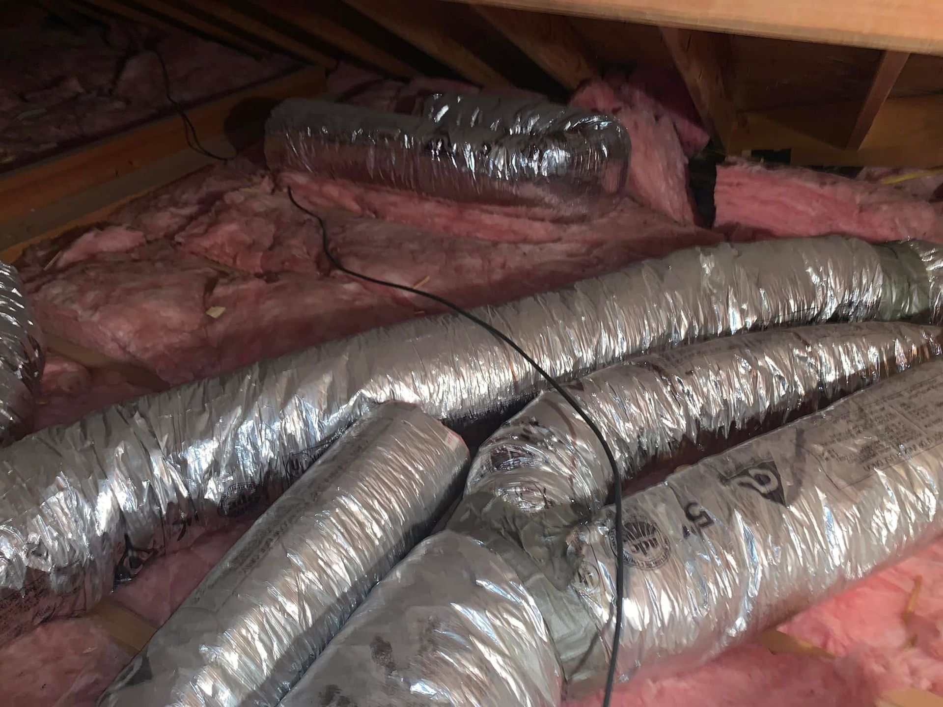Attic crawlspace with silver HVAC ducts over pink insulation