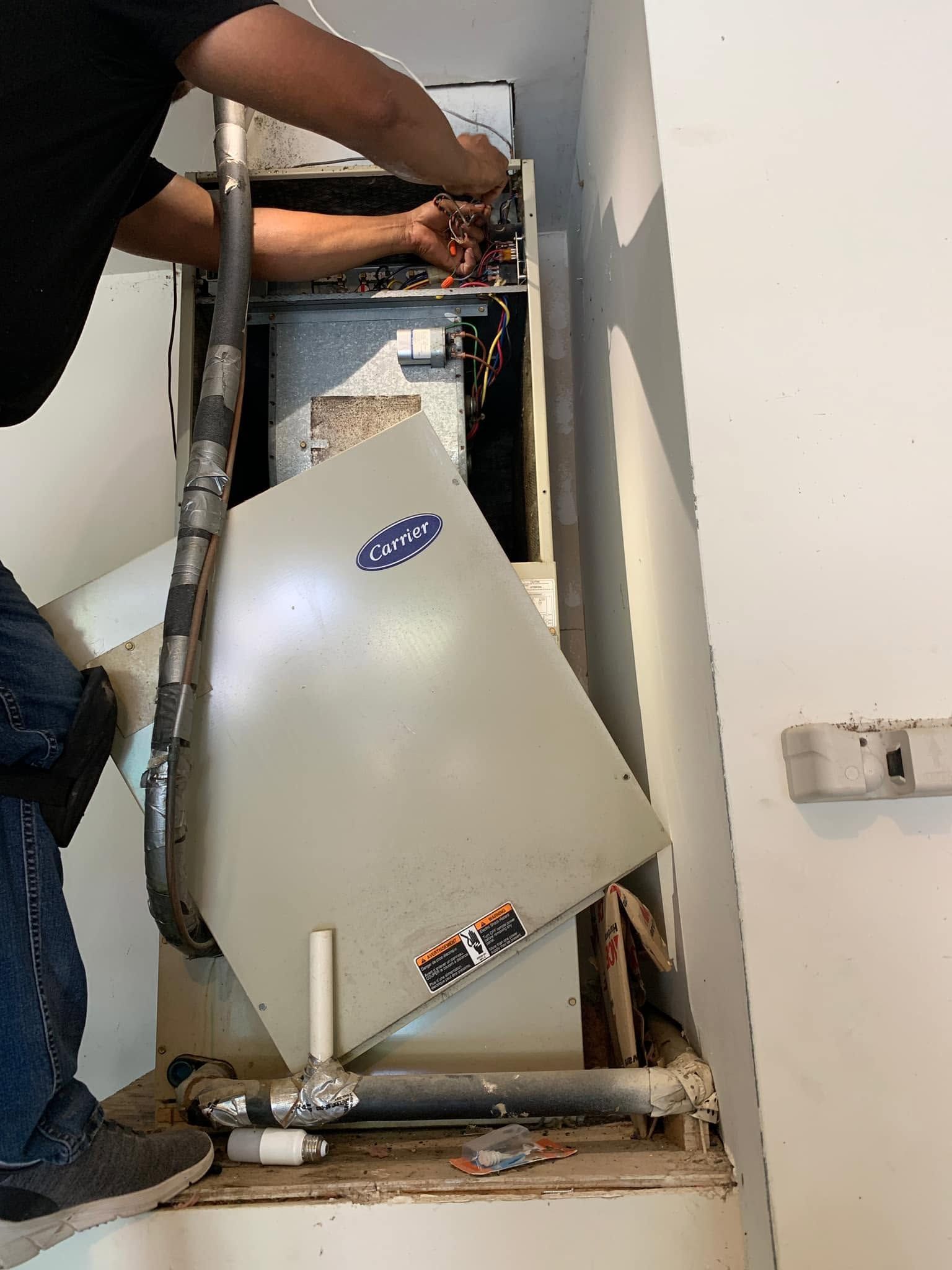 Technician removing a broken white appliance from a wall opening in a hallway