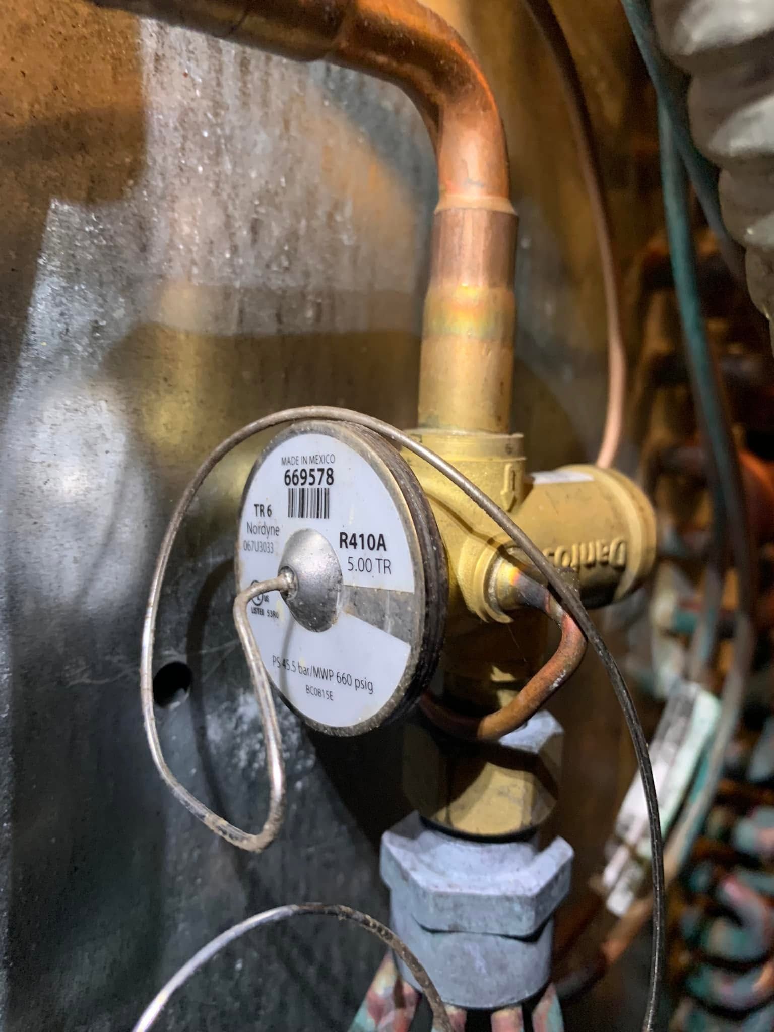 Close-up of a brass valve with a round white gauge and copper pipes in a utility area