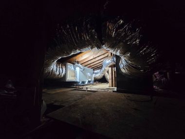 Collapsed roof with debris inside a dark building, lit by a bright opening in the center.