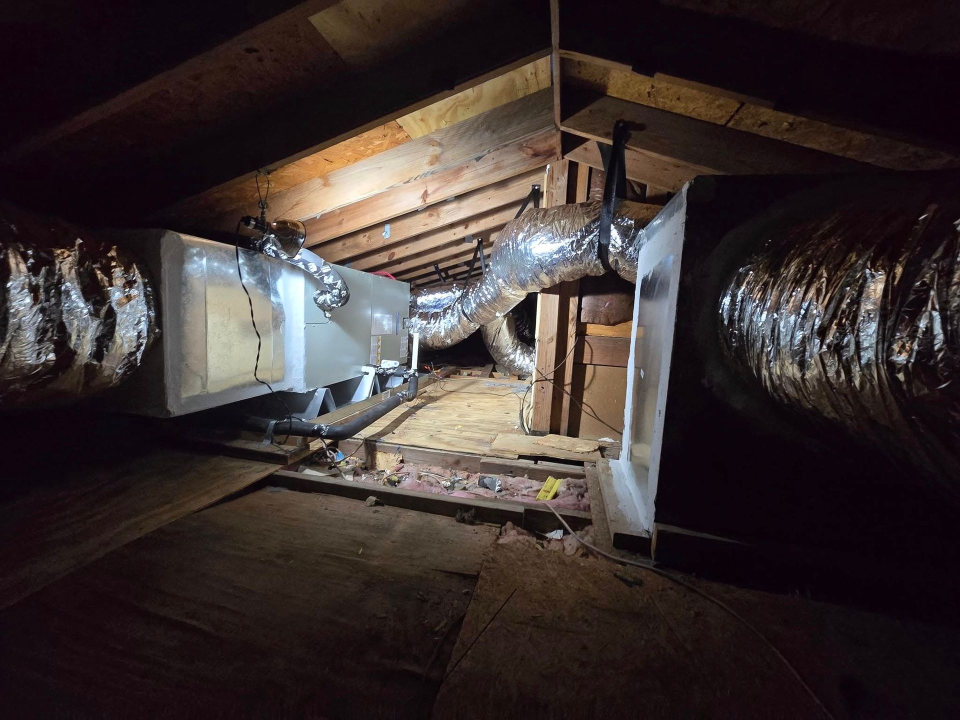 Narrow attic crawlspace with silver ductwork, exposed beams, and insulation under a sloped roof