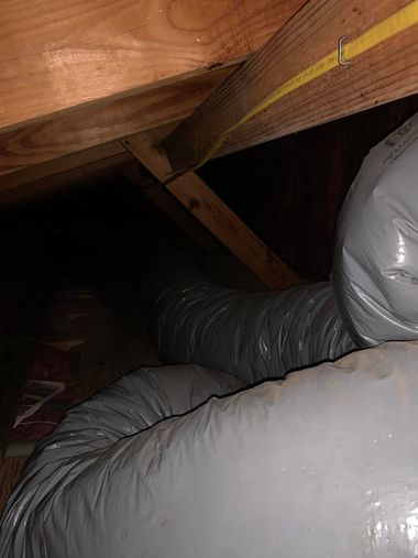 Insulated HVAC ducting and wooden attic rafters inside a dark crawlspace