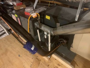 Mechanical ductwork and pipes in an unfinished attic, with orange straps and a blue elbow joint on the floor.