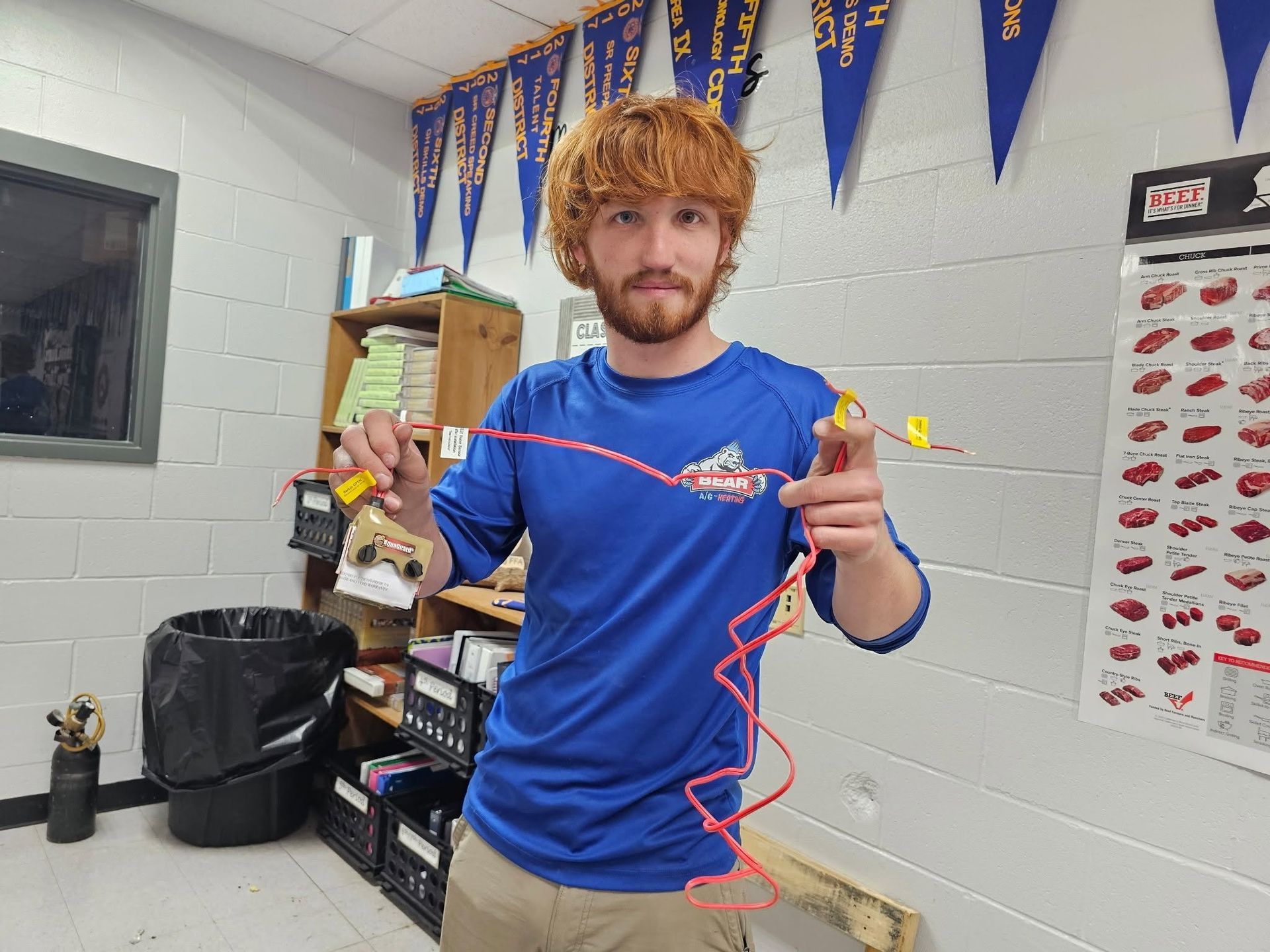 Person in blue shirt holding a red string-lit device in a room with pennants and a bulletin board