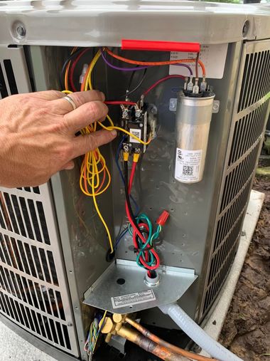 Hand inspecting HVAC unit wiring and capacitor inside an open metal panel.