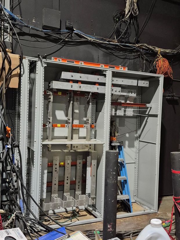 An open, industrial electrical panel cabinet showing internal busbars and mounting hardware in a dark room.