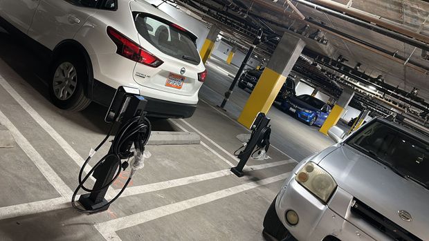A parking garage with two electric vehicle charging stations installed between parked white and silver cars.