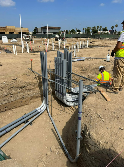 Two workers in high-visibility vests install conduit pipes for electrical wiring at a construction site.