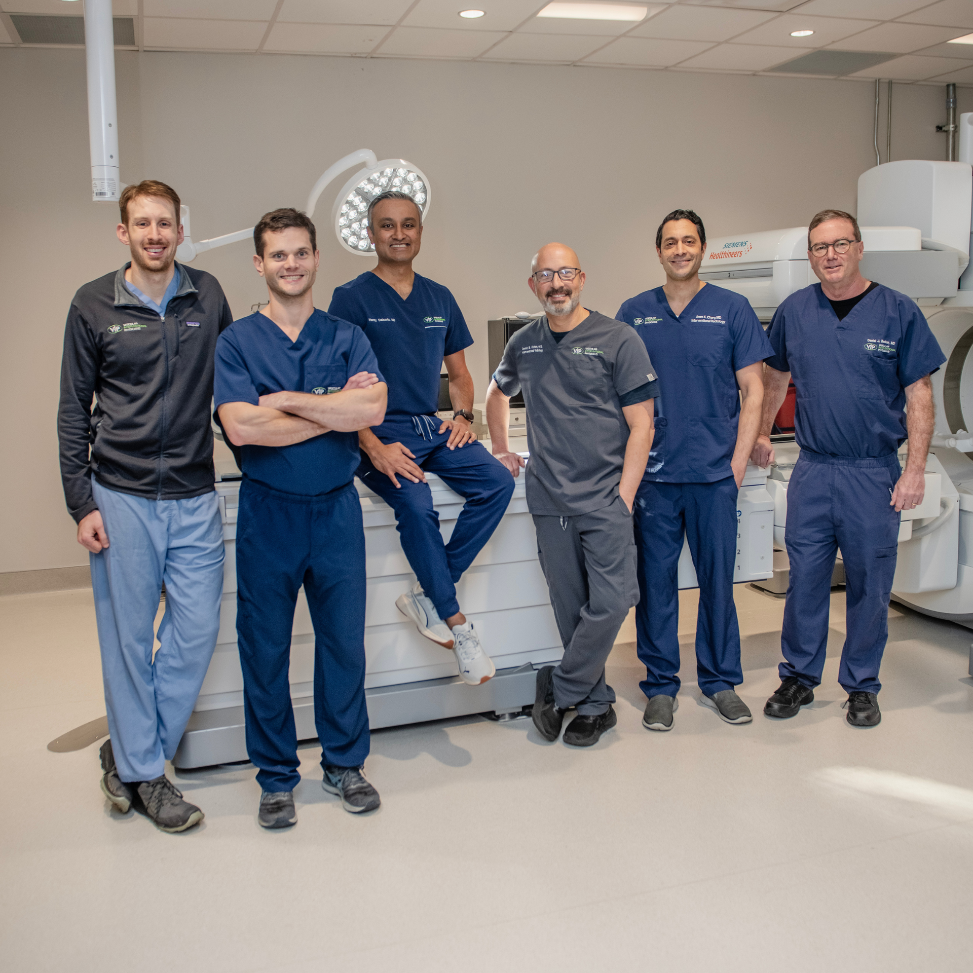 Medical team in scrubs posing near equipment.