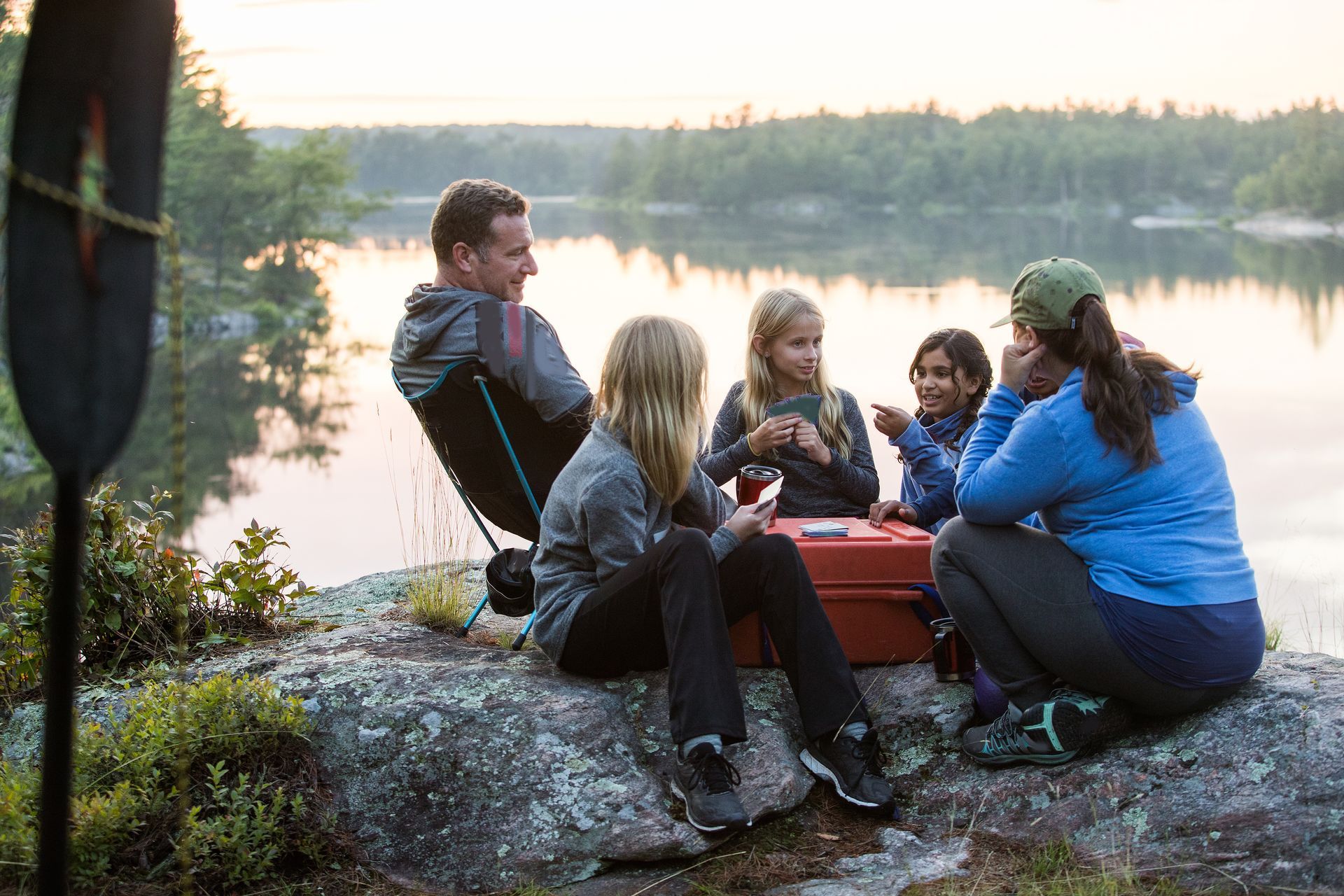 Family sitting by a peaceful lake with camping gear, enjoying the outdoors together