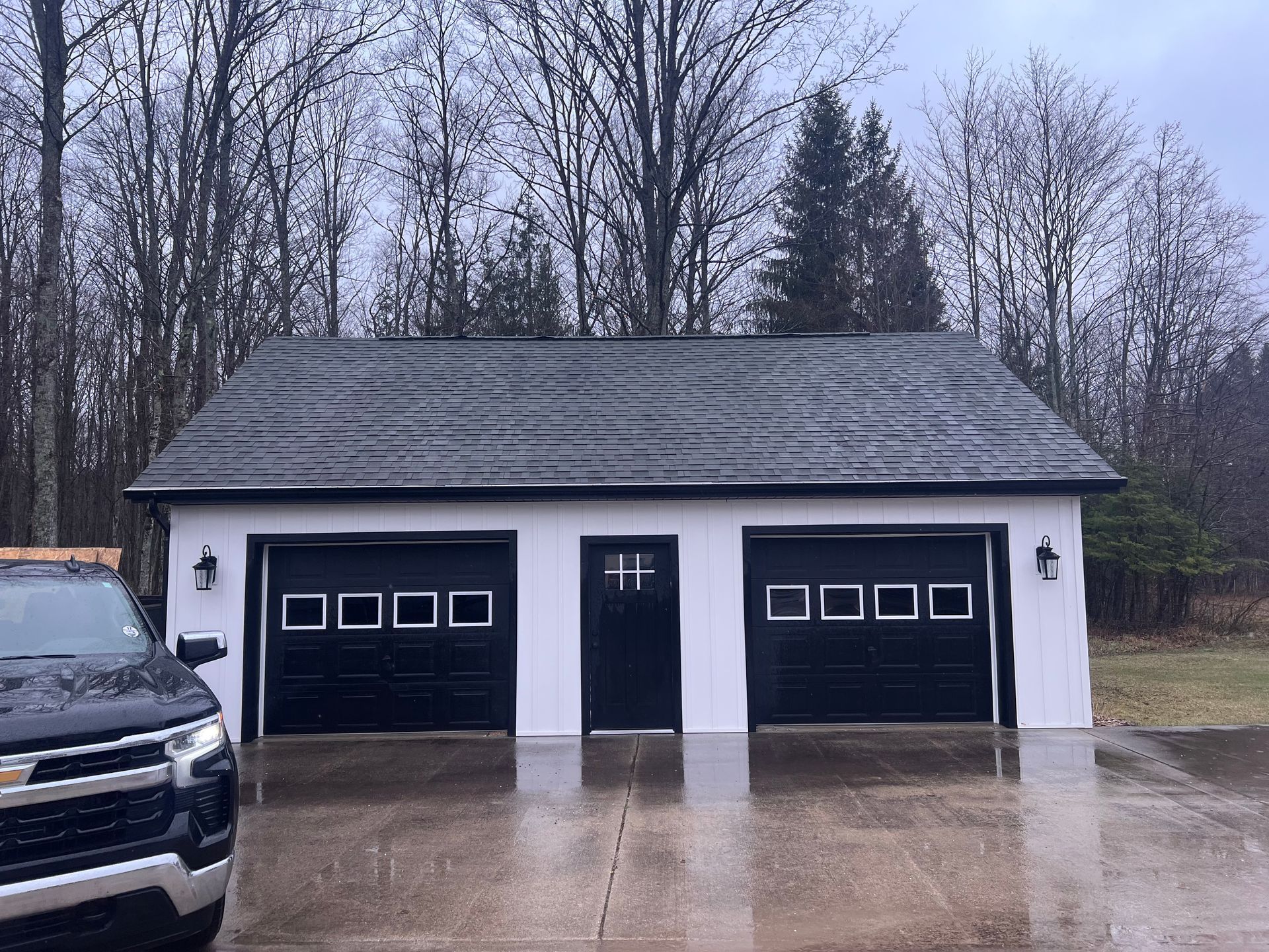 A white shed with two black garage doors and grey asphalt roofing in Gaylord, MI.