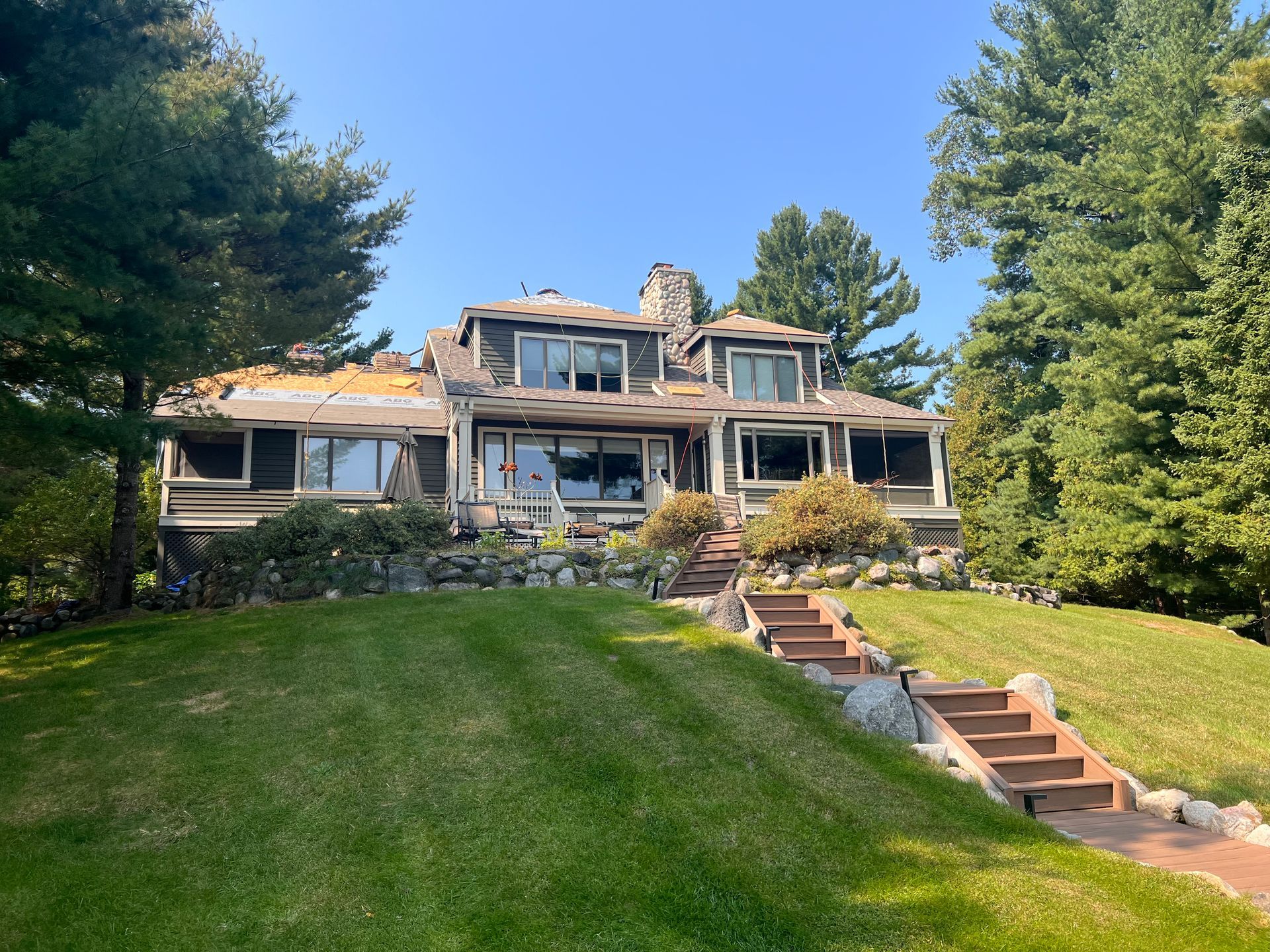 A full view of a lakeside home in Gaylord, Michigan, with a completed shingle roof, well-maintained lawn, and landscaping.