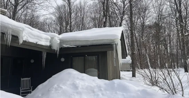 Dark house with thick ice dams on the roof in Gaylord, MI.