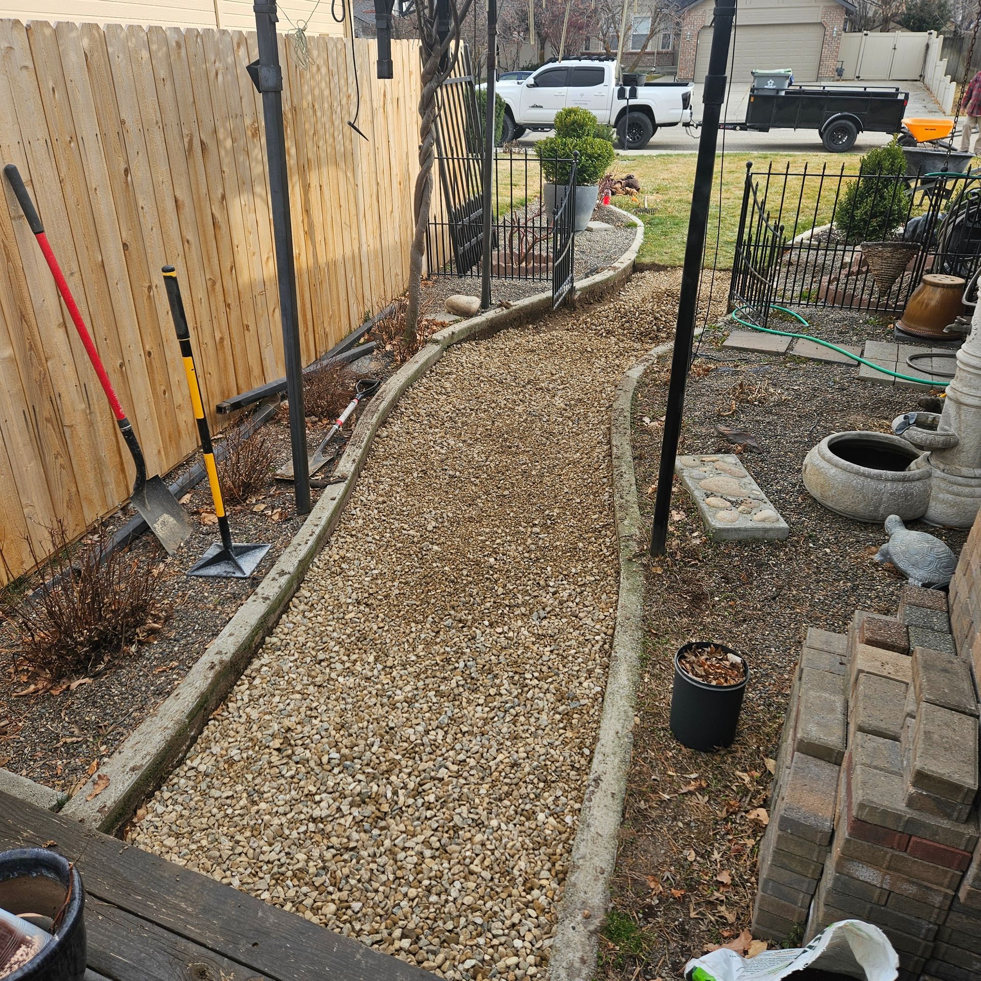 A gravel pathway bordered by concrete, leading through a backyard with a wooden fence and garden.
