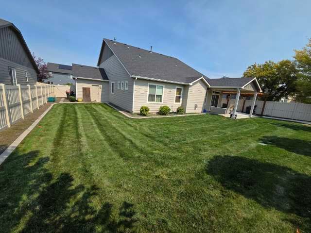 Backyard of a house with manicured green lawn, a covered patio, and a wooden fence on a sunny day.