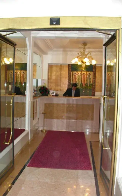 L'ingresso della hall dell'hotel è caratterizzato da porte a vetri, tappeto rosso e banco della reception.