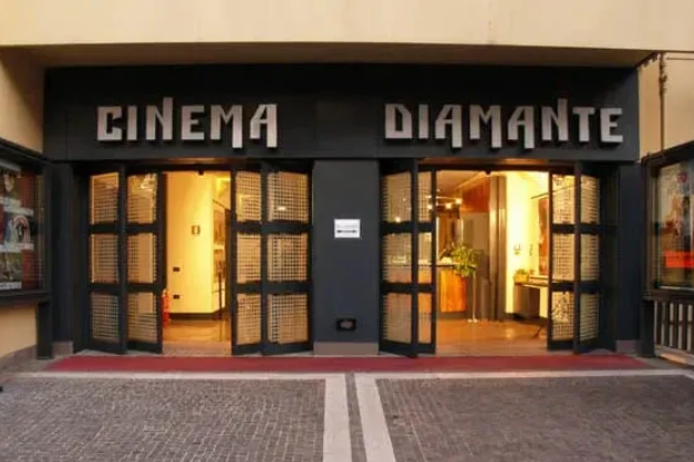 L'ingresso del Cinema Diamante si illumina con le porte e la tenda nera al crepuscolo.