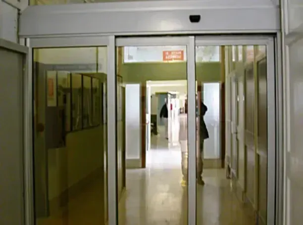 Corridoio vuoto di un aeroporto o di un ospedale con porte scorrevoli in vetro e una persona in lontananza.