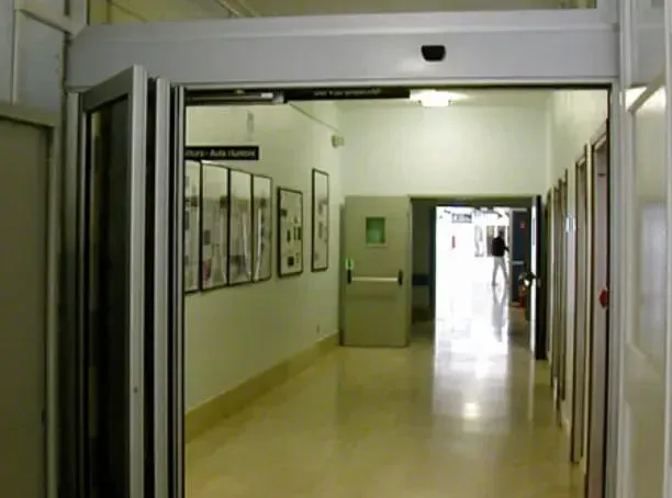 Corridoio vuoto dell'ospedale con quadri incorniciati, pareti bianche e una luce intensa in fondo.