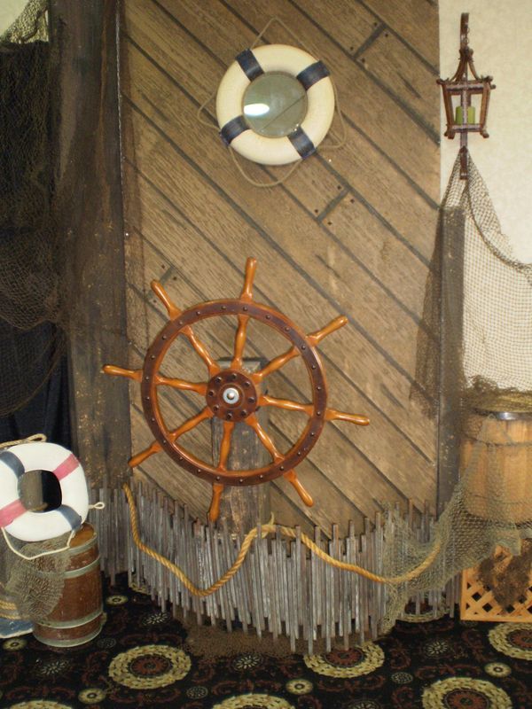 A life preserver is hanging on a wooden wall next to a steering wheel