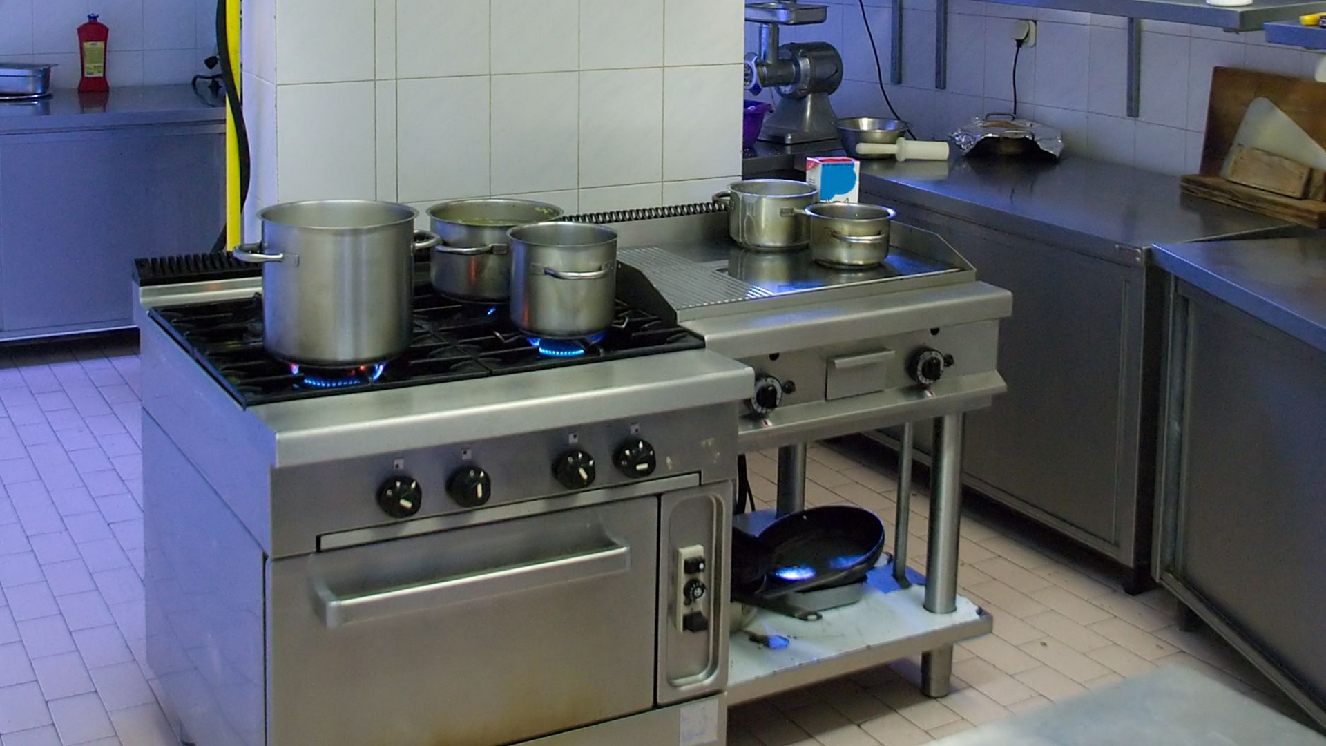 Commercial kitchen hood installation in a well-equipped kitchen with stainless steel appliances. Commercial kitchen hood installation in a well-equipped kitchen with stainless steel appliances.