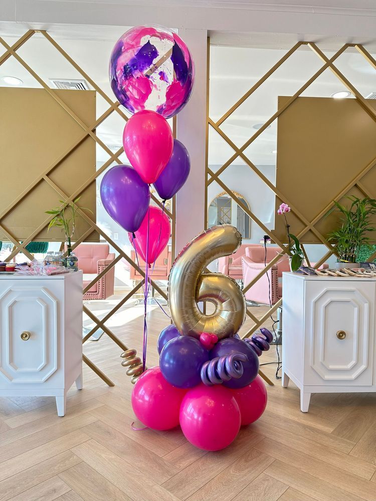 Balloon display with a gold number 6, featuring pink, purple, and a marbled top balloon in a room with a gold geometric wall.