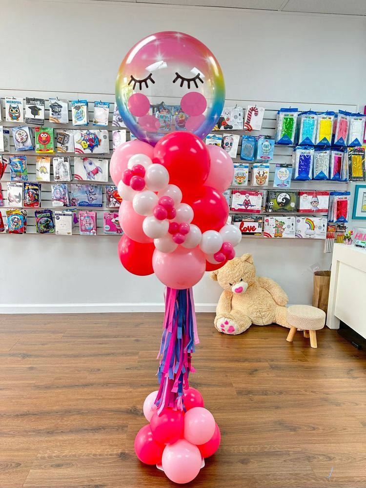 Balloon centerpiece with rainbow cloud top, pink and red balloons, and tassels.