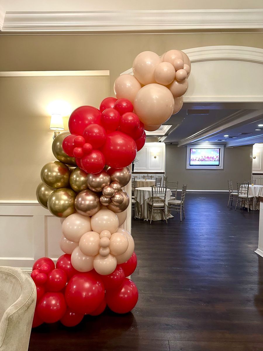 Balloon arch in red, gold, and nude colors, framing an event space entrance.