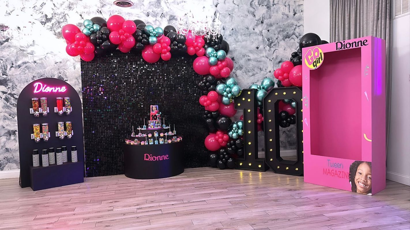 Party decorations, including balloons, backdrops, and a display stand with the name