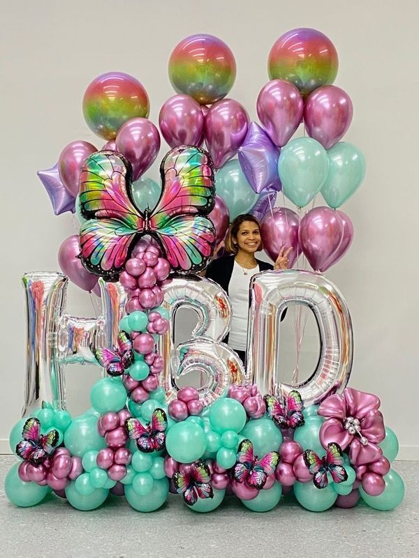 Girl smiles behind a colorful balloon arrangement that spells