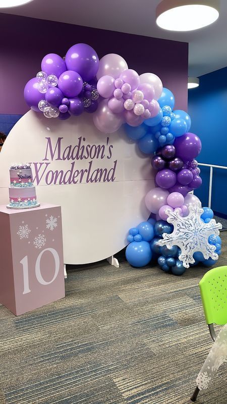 A party scene with a balloon arch in shades of purple and blue, 
