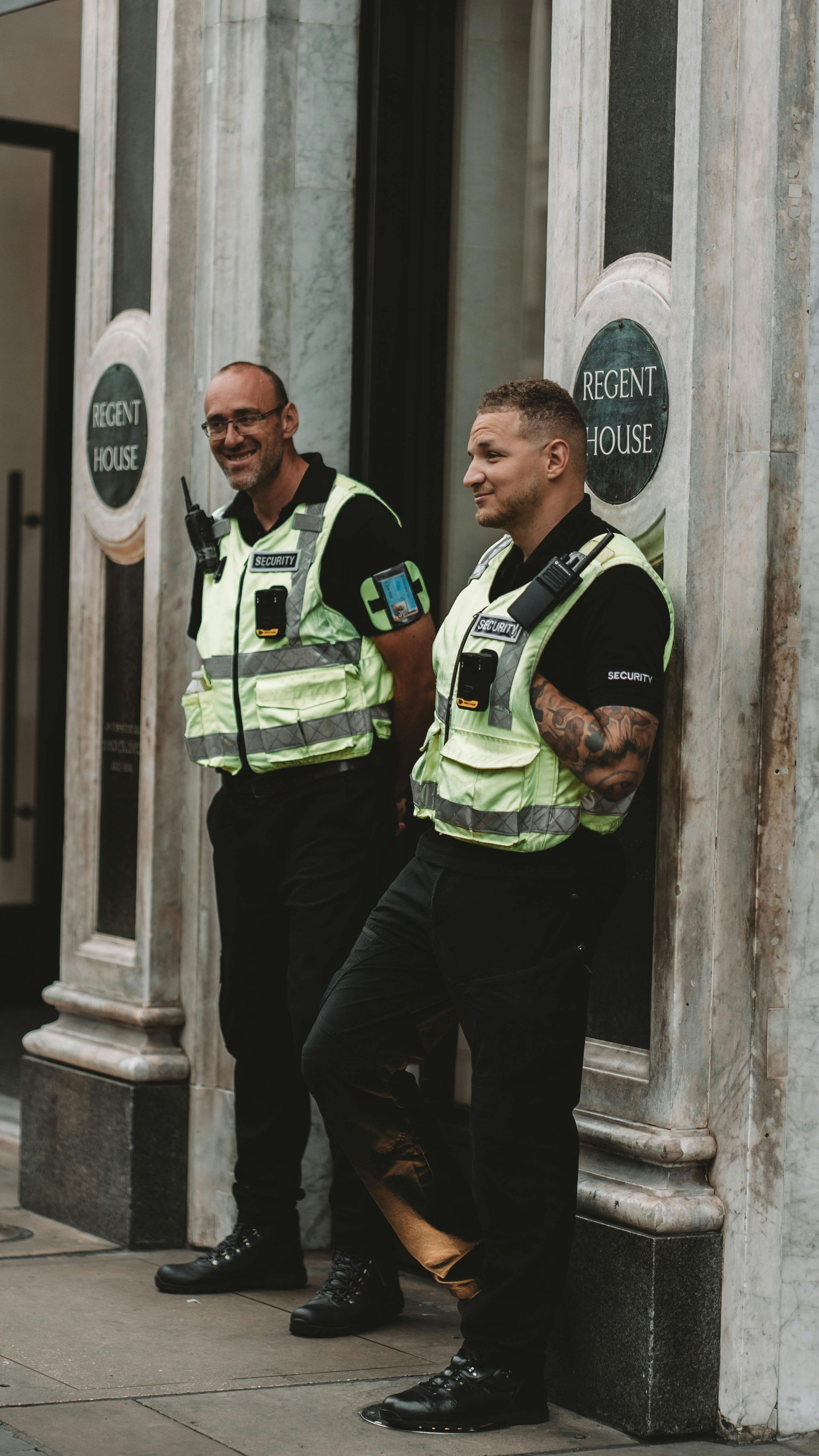 Two police officers in vests stand outside a building, smiling.