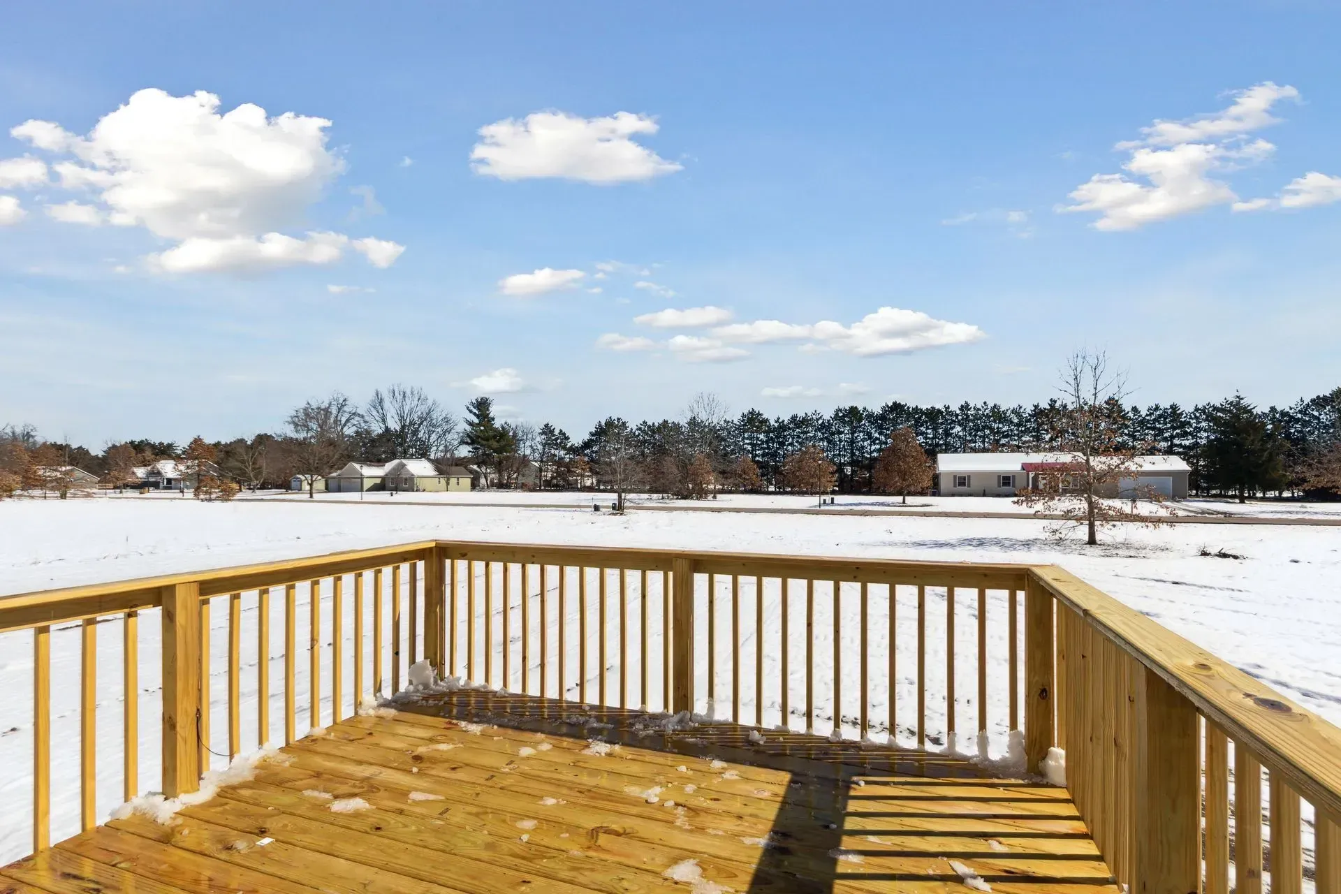 Wooden deck overlooking a snowy field under a blue sky with clouds