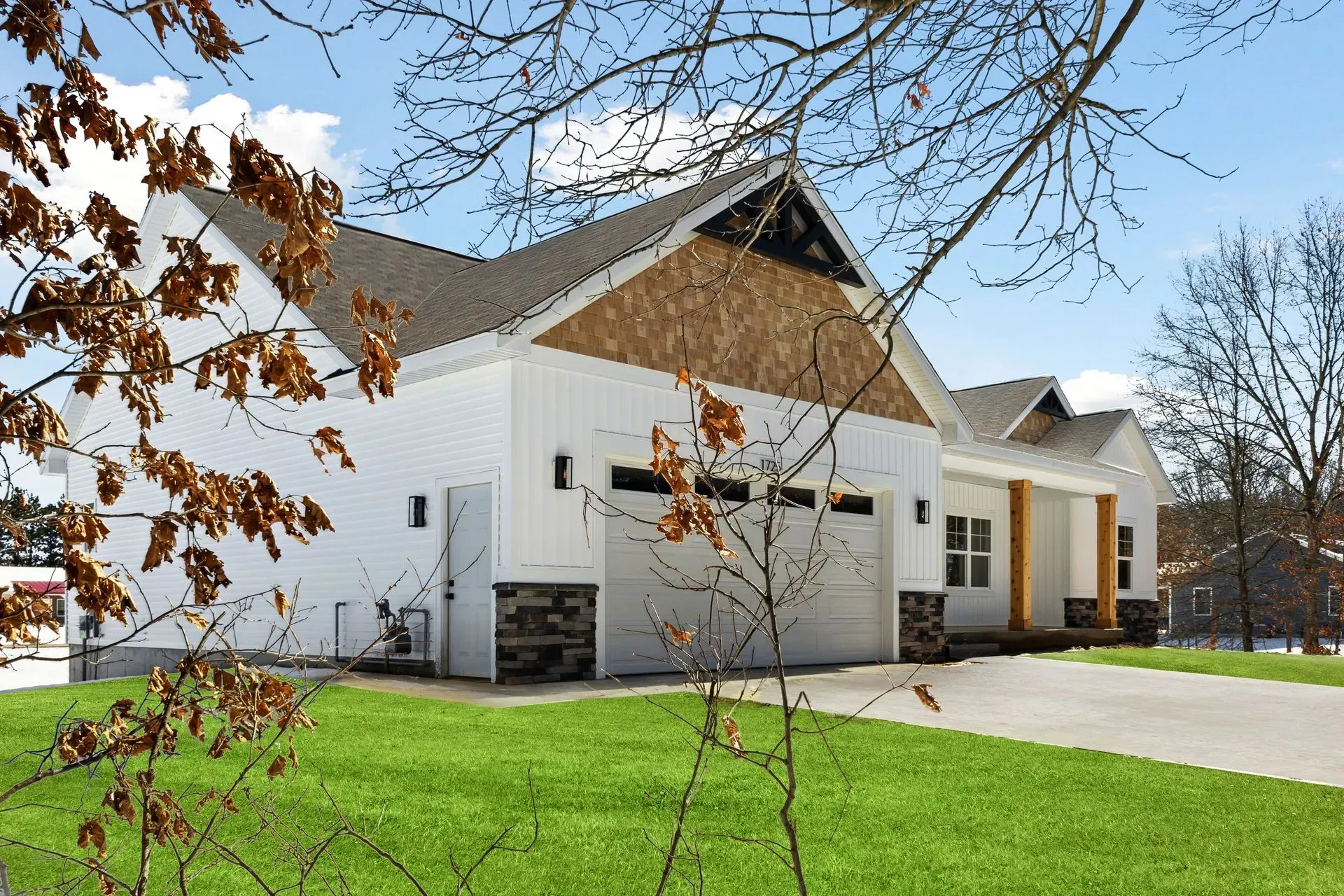 White suburban house with a two-car garage, green lawn, and bare tree branches in front