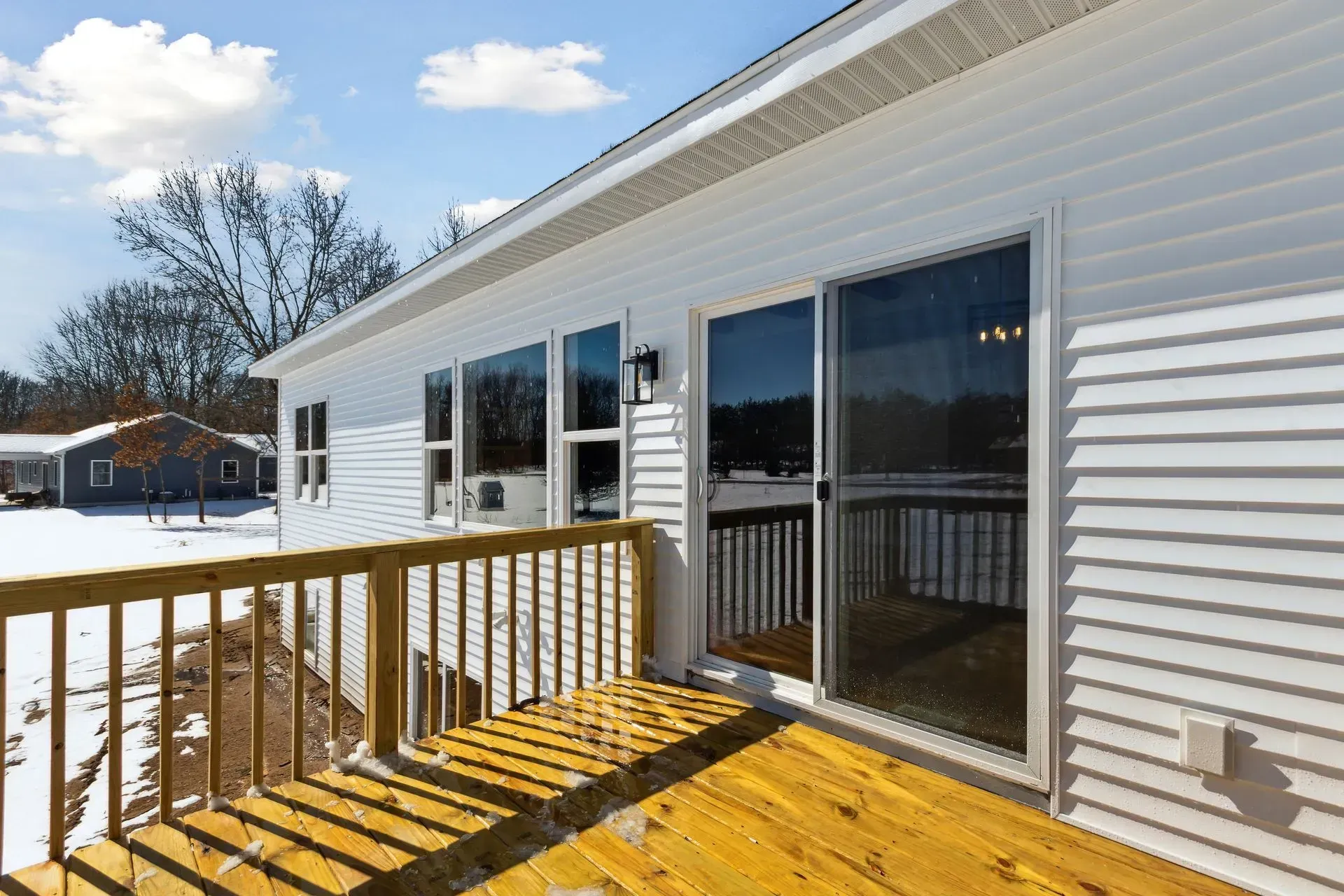 Snowy backyard deck beside a white house with sliding glass doors and wooden railing